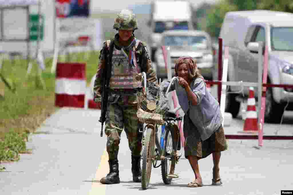 A woman pushes her bicycle through a checkpoint manned by Thai security forces in the troubled southern province of Yala, Thailand.