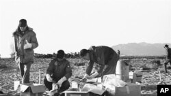 FILE - Technicians of the U.S. Air Force use rubber gloves while picking up pieces of the wreckage and placing them in cardboard boxes in Palomares, Spain, Jan. 28, 1966. 