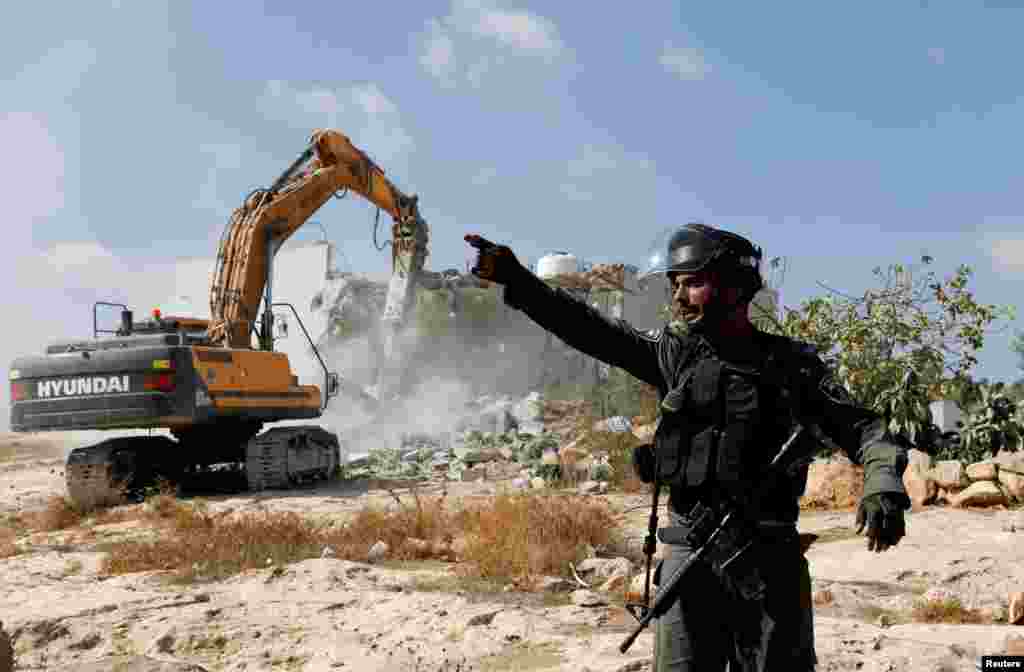 An Israeli border police officer gestures as machinery demolishes a Palestinian house near Yatta, in the Israeli-occupied West Bank.
