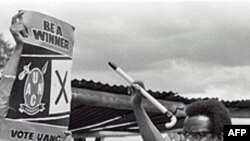 Bishop Abel Muzorewa, member of executive council and leader of UANC, shows voters how to vote by signing a cross near crest of his party during Rhodesian general elections, 19 Apr 1979 