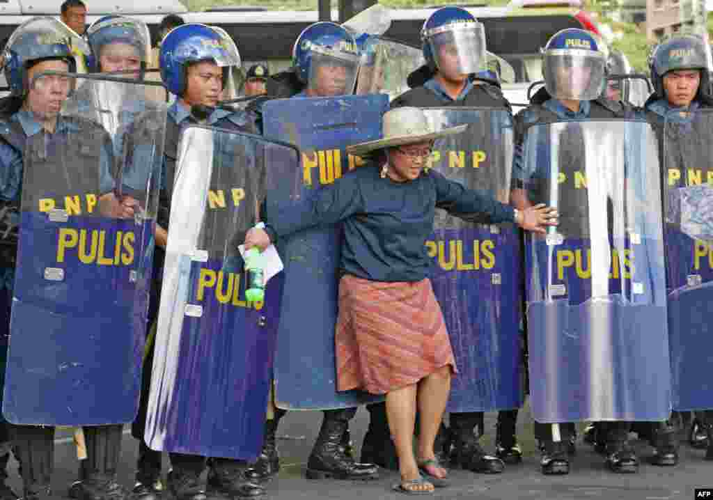 Seorang perempuan berdiri di depan barisan polisi dalam bentrokan antara buruh demonstran dan polisi di Makati, Manila (16/11), di tengah protes untuk mengemukakan isu-isu tenaga kerja saat berlangsungnya KTT APEC. (AFP/Joseph Agcaoili)