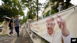 People walk past in front of a poster with a photo of Pope Francis ahead of his visit to Singapore on the street in Singapore, Sept. 10, 2024.