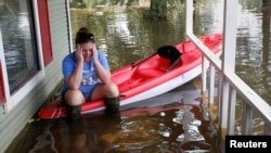 A woman sits on a kayak that is floating on her friend's porch as the house is cleaned of possessions after Tropical Storm Harvey in Orange, Texas, Sept. 1, 2017. 