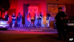 Bystanders watch outside boarded-up shops as protesters clash with police late Tuesday, Aug. 25, 2020, in Kenosha, Wis. Protests continued following the police shooting of Jacob Blake two days earlier. (AP Photo/David Goldman)