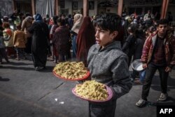 FILE - A displaced Palestinian child holds plates of food at a government school in Rafah in the southern Gaza Strip on February 19, 2024.