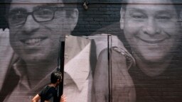 Seseorang melangkah melalui pintu yang ditutupi oleh mural yang menggambarkan sandera Amerika dan tahanan yang salah yang ditahan di luar negeri, Rabu, 20 Juli 2022, di Georgetown di Washington. (Foto: AP)