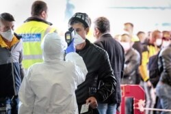 An airport employee checks the temperature of a Romanian seasonal worker at the Avram Iancu international airport, in Cluj, Romania, April 9, 2020. More then 1,800 workers from Romania are traveling to Germany, most to work in asparagus farms.