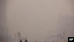 Pedestrians walk along a square as a security guard stands nearby on a hazy day in Beijing January 18, 2012.