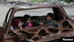 Children play inside the wreckage of a burnt vehicle at al-Myassar neighborhood in Aleppo, Syria, Feb. 16, 2015. 