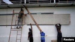 Workers protect the windows of a bar in anticipation of Tropical Storm Laura's arrival, in Havana, Cuba, Aug. 24, 2020. 