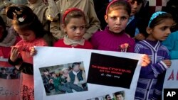 FILE - Pakistani children hold a placard showing pictures of Peshawar's school attack victims during a demonstration in connection with first anniversary of the school attack, Dec. 15, 2015.