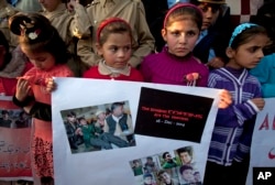 Pakistani children hold a placard showing pictures of Peshawar's school attack victims during a demonstration in connection with first anniversary of the school attack, Dec. 15, 2015.