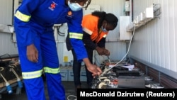 Des employés chargent les batteries lithium-ion d'une moto électrique dans une station de recharge à énergie solaire à Wedza, au Zimbabwe, le 22 mai 2020.