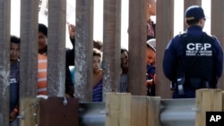 FILE - Migrants from Central America look through a border wall as a U.S. Customs and Border Protection officer, right, stands on the other side Nov. 25, 2018.