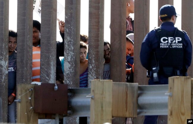 2018年11月25日在美国加州圣迭戈的边界栅栏两侧，有美国海关和边境保护局人员和企图进入美国的移民。