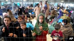 Children stand behind a fence in a hangar as they wait for their departure at the Ramstein U.S. Air Base in Ramstein, Germany, Aug. 30, 2021, where the American military community overseas houses thousands Afghan evacuees in a tent city at this airbase.