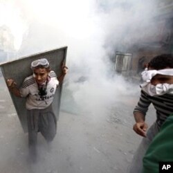 埃及警方11月23 日在解放廣場附近發放催淚瓦斯，一名示威者以金屬牌作防護