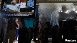 File - People line up to enter the Extraordinary Chambers in the Courts of Cambodia as a television screen shows former Khmer Rouge president Khieu Samphan, in Phnom Penh.