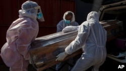Des croque-morts en tenue de protection portent le cercueil d'une femme décédée du Covid-19 dans un corbillard à Katlehong, près de Johannesburg en Afrique du Sud, le 21 juillet 2020. 