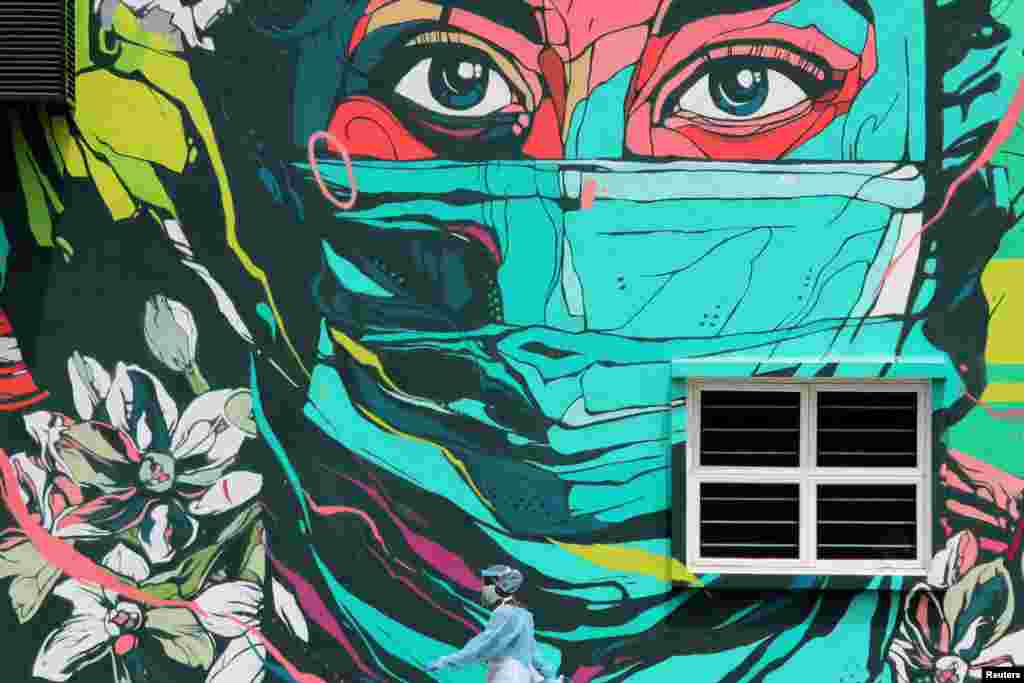 A medical worker wearing personal protective equipment passes by a mural outside a clinic, amid the coronavirus outbreak in Kuala Lumpur, Malaysia.