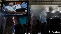 People line up to enter the Extraordinary Chambers in the Courts of Cambodia as a television screen shows former Khmer Rouge president Khieu Samphan, near Phnom Penh, October 21, 2013. 