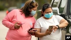 Dos mujeres caminando con sus rostros cubiertos mientras consultan con sus teléfonos inteligentes en Houston, Texas.