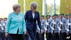 German Chancellor Angela Merkel, left, and British Prime Minister Theresa May walk on the red carpet during a military welcoming ceremony at the chancellery in Berlin Wednesday, July 20, 2016, on May's first foreign trip after being named British prime minister. 