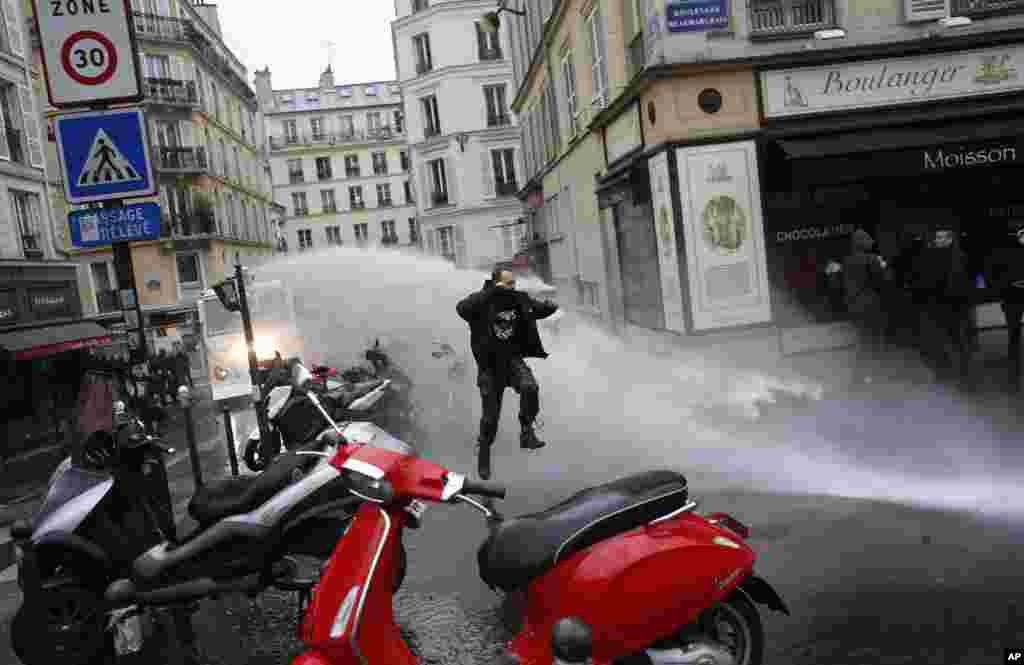 A man jumps to avoid a police water canon during a demonstration in Paris, France. Nationwide strikes caused major disruptions to trains, planes, schools and other public services as unions set up dozens of street protests across the country.