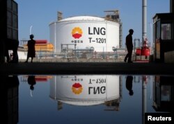 Tangki penyimpanan gas alam cair (LNG) dan pekerja tercermin dalam genangan air di terminal penerima PetroChina di Pelabuhan Rudong di Nantong, Provinsi Jiangsu, China, 4 September 2018. (Foto: Reuters)