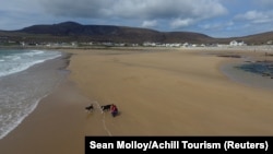 A woman walks her dogs along Dooagh beach after a storm returned sand to it, 30 years after another storm had stripped all the sand off the beach, on Achill island, County Mayo, Ireland, May 5, 2017.