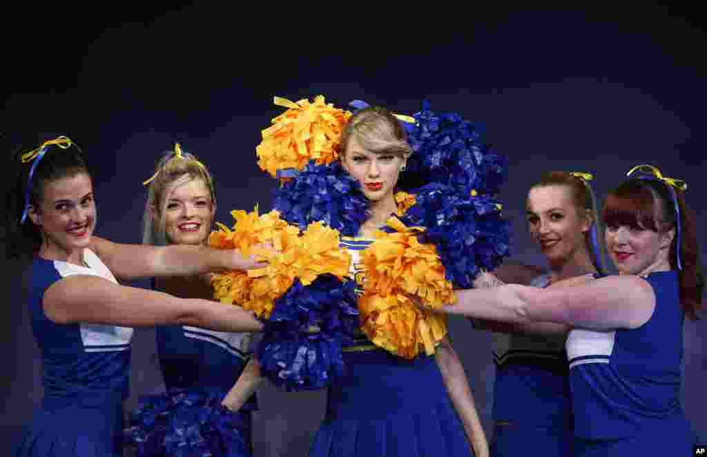 Dancers in cheerleader costumes pose for the photographers next to a wax figure of U.S. singer Taylor Swift during a photo call in central London. The new wax figure was unveiled at the Madame Tussauds London attraction.
