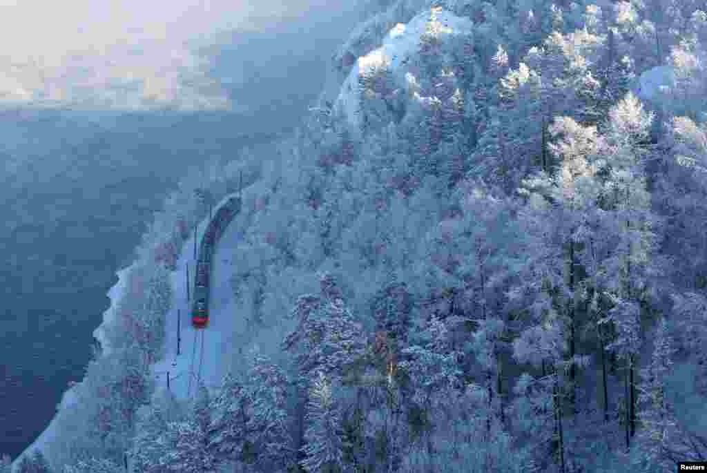 A passenger train moves along the bank of the Yenisei River in the Siberian Taiga forest covered with snow, outside Krasnoyarsk, Russia.