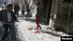 People inspect the damage as a civilian walks near blood stains at a market hit by air strikes in Aleppo's rebel-held al-Fardous district, Syria, Oct. 12, 2016. 