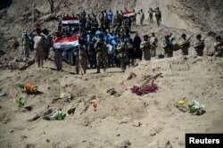 FILE- Iraqi soldiers salute the mass grave for Shi'ite soldiers from Camp Speicher who were killed by Islamic State militants in the presidential compound of the former Iraqi president Saddam Hussein in Tikrit, April 6, 2015.