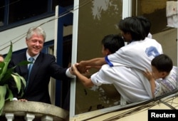 FILE - Then-President Bill Clinton shakes hands with a group of children hanging out of a window in their residence in Hanoi, Vietnam, Nov. 17, 2000.