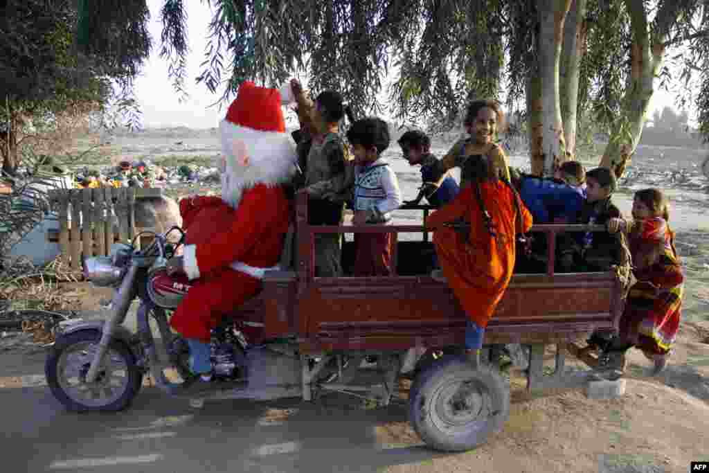 A man dressed in a Santa Claus outfit takes children on a ride in a tuktuk on the outskirts of the Iraqi central city of Najaf.
