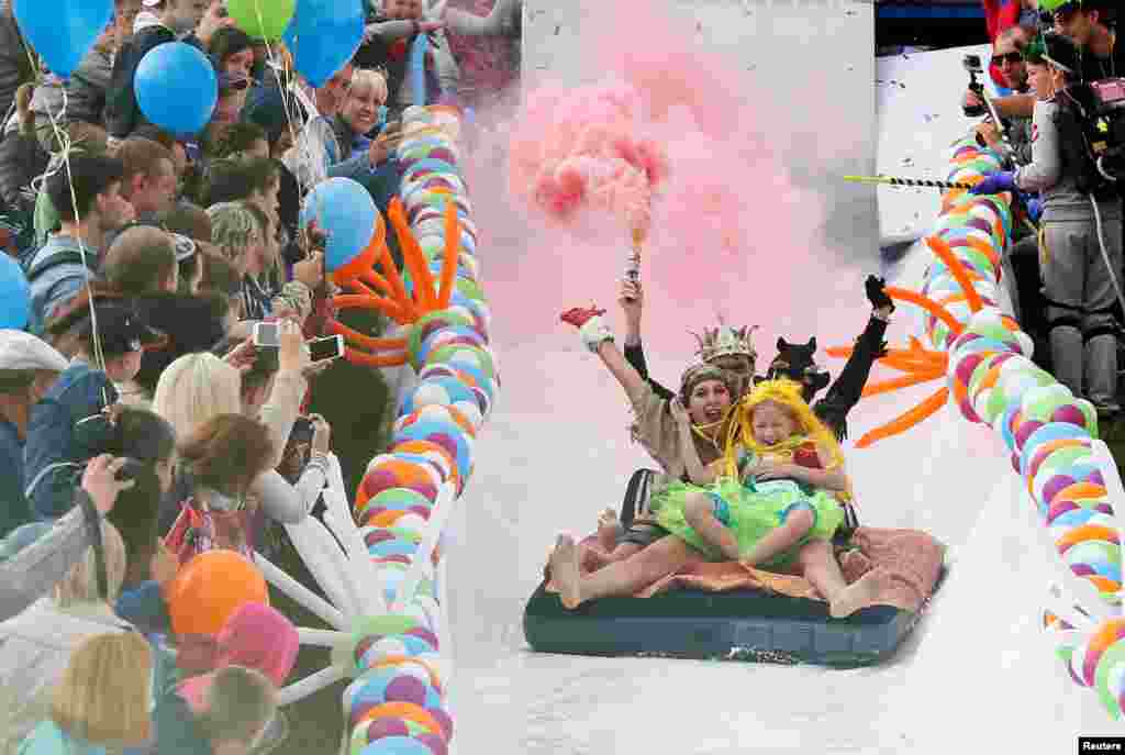 Participants hold smoke flares as they slide down along a chute to cross a pool of water and foam during the &quot;Letniy Gornoluzhnik&quot; (Summer mountain puddle rider) festival at the Bobroviy Log Fun Park near the Siberian city of Krasnoyarsk, Russia.