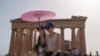 FILE - Tourists with an umbrella walk in front of the Parthenon at the ancient Acropolis in central Athens, June 12, 2024. 