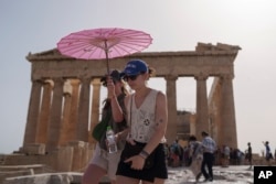 Turis membawa payung berjalan di depan Parthenon di Acropolis kuno di pusat Athena, 12 Juni 2024. Juni 2024 merupakan Juni terpanas yang pernah tercatat, menurut layanan iklim Copernicus Eropa pada Senin, 8 Juli. (Foto: AP)