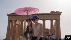 FILE - Tourists with an umbrella walk in front of the Parthenon at the ancient Acropolis in central Athens, June 12, 2024. 