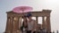 FILE - Tourists with an umbrella walk in front of the Parthenon at the ancient Acropolis in central Athens, June 12, 2024. 