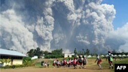 Anak-anak sekolah SD Sipandak di desa Tiga Pancur berjalan bersama sementara gunung Sinabung memuntahkan abu vulkanik di belakang, Senin (19/2). 