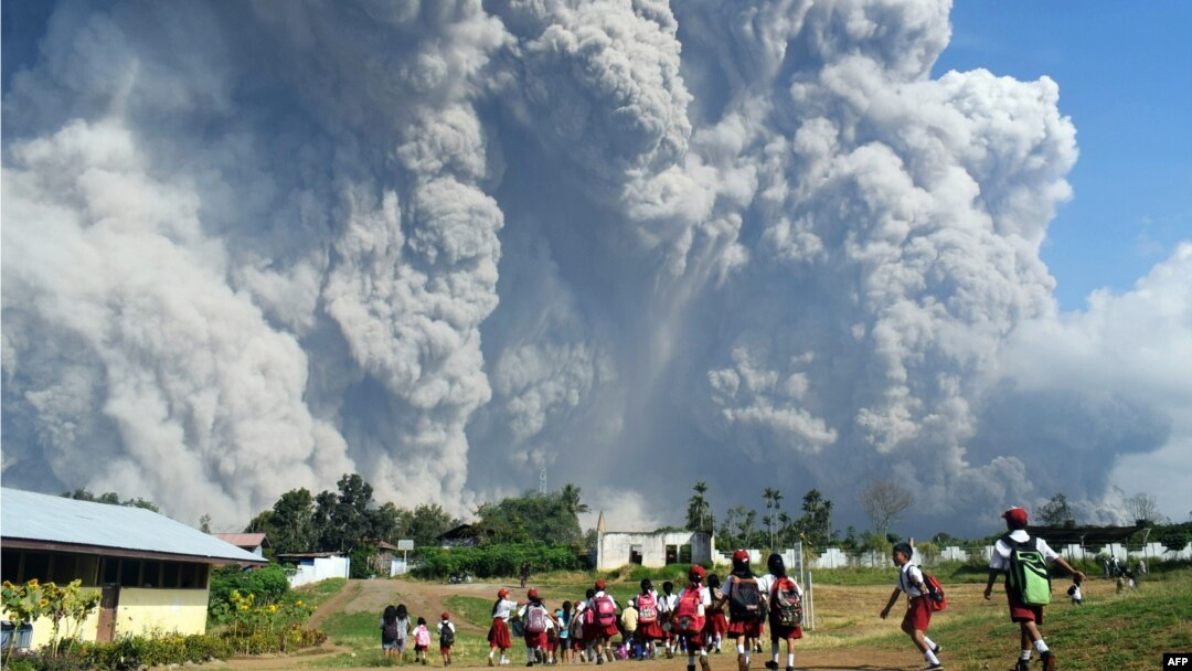 Anak-anak sekolah dasar berjalan bersama di SD Sipandak, Desa Tiga Pancur, di Karo, Sumatra Utara, sementara awan abu tebal menyembur dari Gunung Sinabung, 19 Februari 2018.
