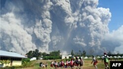 Anak-anak sekolah dasar berjalan bersama di SD Sipandak, Desa Tiga Pancur, di Karo, Sumatra Utara, sementara awan abu tebal menyembur dari Gunung Sinabung, 19 Februari 2018.