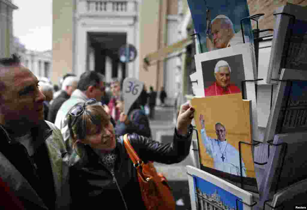 Turisti razgledaju fotografije novo-izabarnog pape Francisa u jednoj od prodavnica suvenira u blizini Vatikana. A ako tako odluče, mogu kupiti i lijepu fotografiju prethodnog pape.