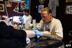 Tattoo artists ink designs on customers during a session at The Rembrandt House Museum in Amsterdam on June 19, 2023. (Photo by SIMON WOHLFAHRT / AFP)