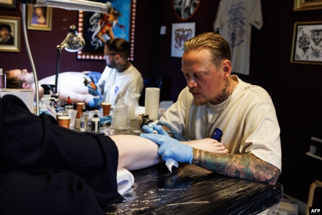 Tattoo artists ink designs on customers during a session at The Rembrandt House Museum in Amsterdam on June 19, 2023. (Photo by SIMON WOHLFAHRT / AFP)