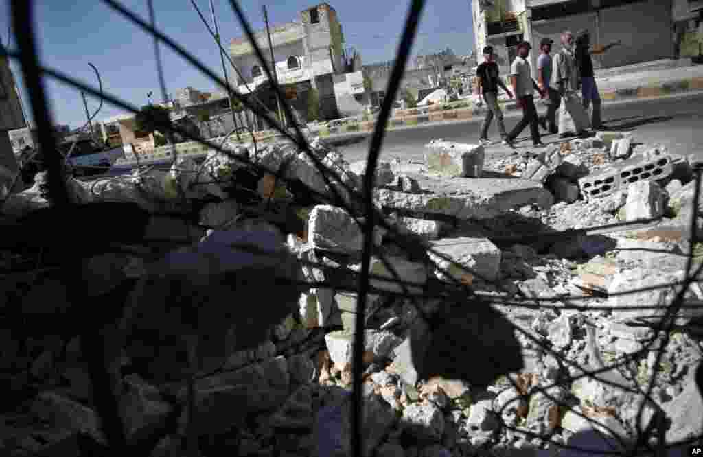 In this August 5, 2012 photograph, Syrians pass by a destroyed house in town of Atareb outskirts of Aleppo, Syria.