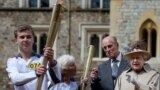 Britain's Queen Elizabeth (R), Prince Philip (2nd R), and Olympic torch bearer Gina Macgregor (2nd L) watch as torchbearer Phil Wells takes the Olympic Flame at Windsor Castle, west of London July 10, 2012. 