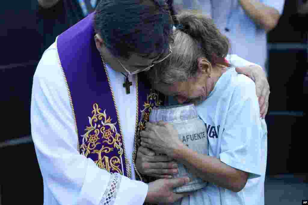 O sacerdote católico filipino Flavie Villanueva, à esquerda, consola Melinda Lafuente enquanto esta segura a urna que contém os restos mortais do seu filho Angelo, durante uma cerimónia de enterro para vítimas de execuções extrajudiciais, na cidade de Caloocan, nas Filipinas.